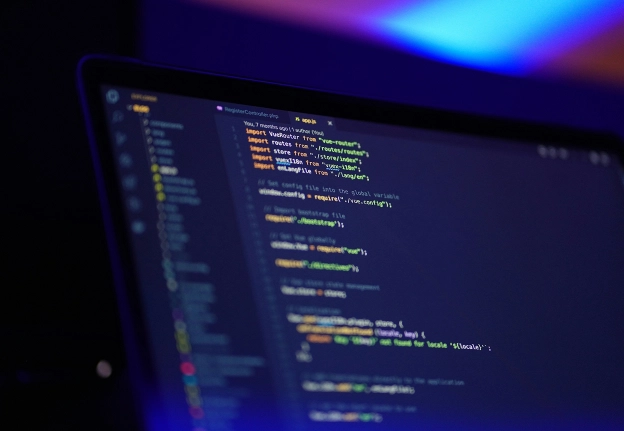 Écran d’ordinateur portable affichant du code informatique coloré dans un éditeur, sous un éclairage bleu et violet tamisé.