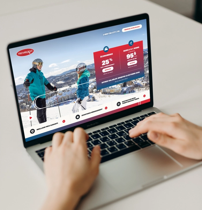 Une personne utilise un ordinateur portable affichant une page Web promotionnelle sur le ski, avec deux skieurs sur une piste enneigée et des offres mises en évidence en rouge.